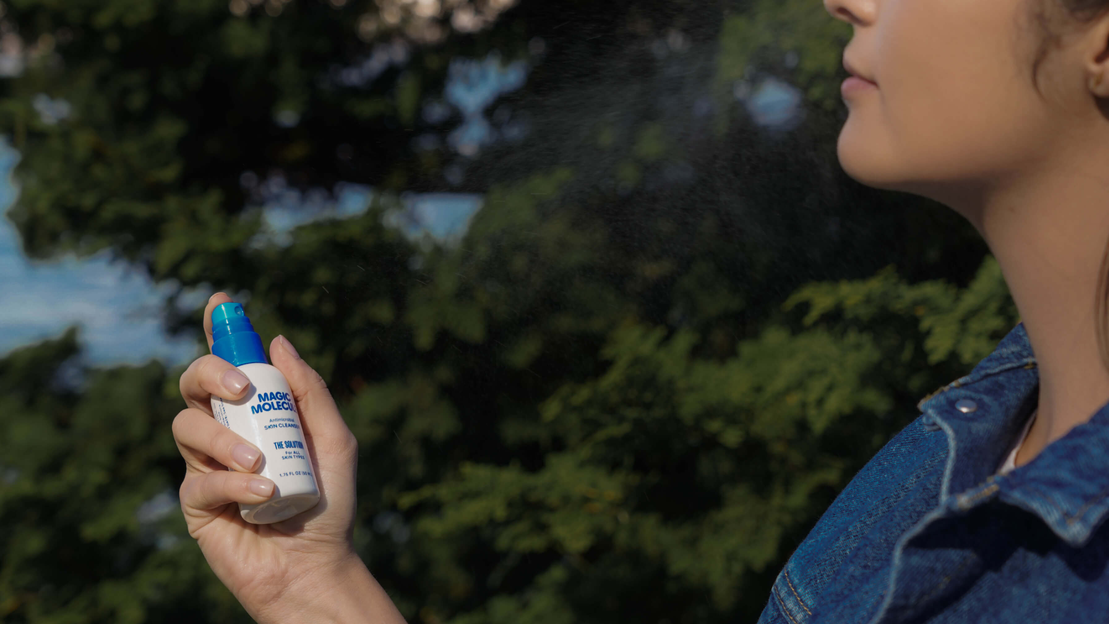 Person spraying Magic Molecule on their face outside